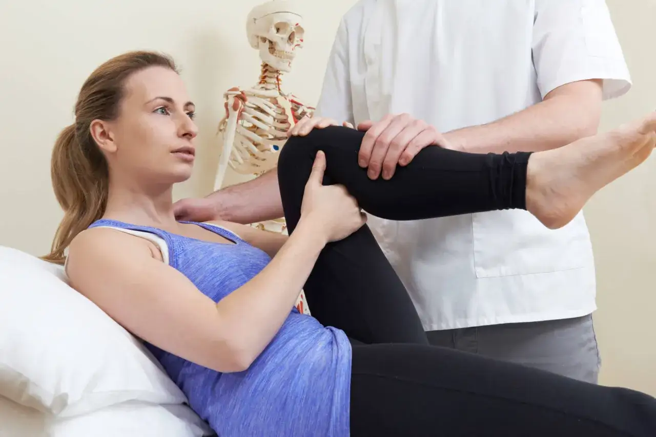 Fizjoterapeuta bada kolano pacjentki, która odczuwa promieniujący ból kolana. W tle widoczny szkielet.