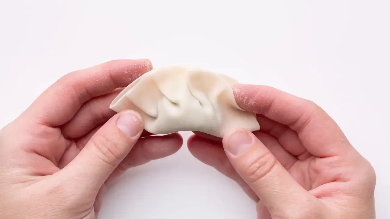 Händer som formar en dumpling, redo för ett gott dumplings recept.