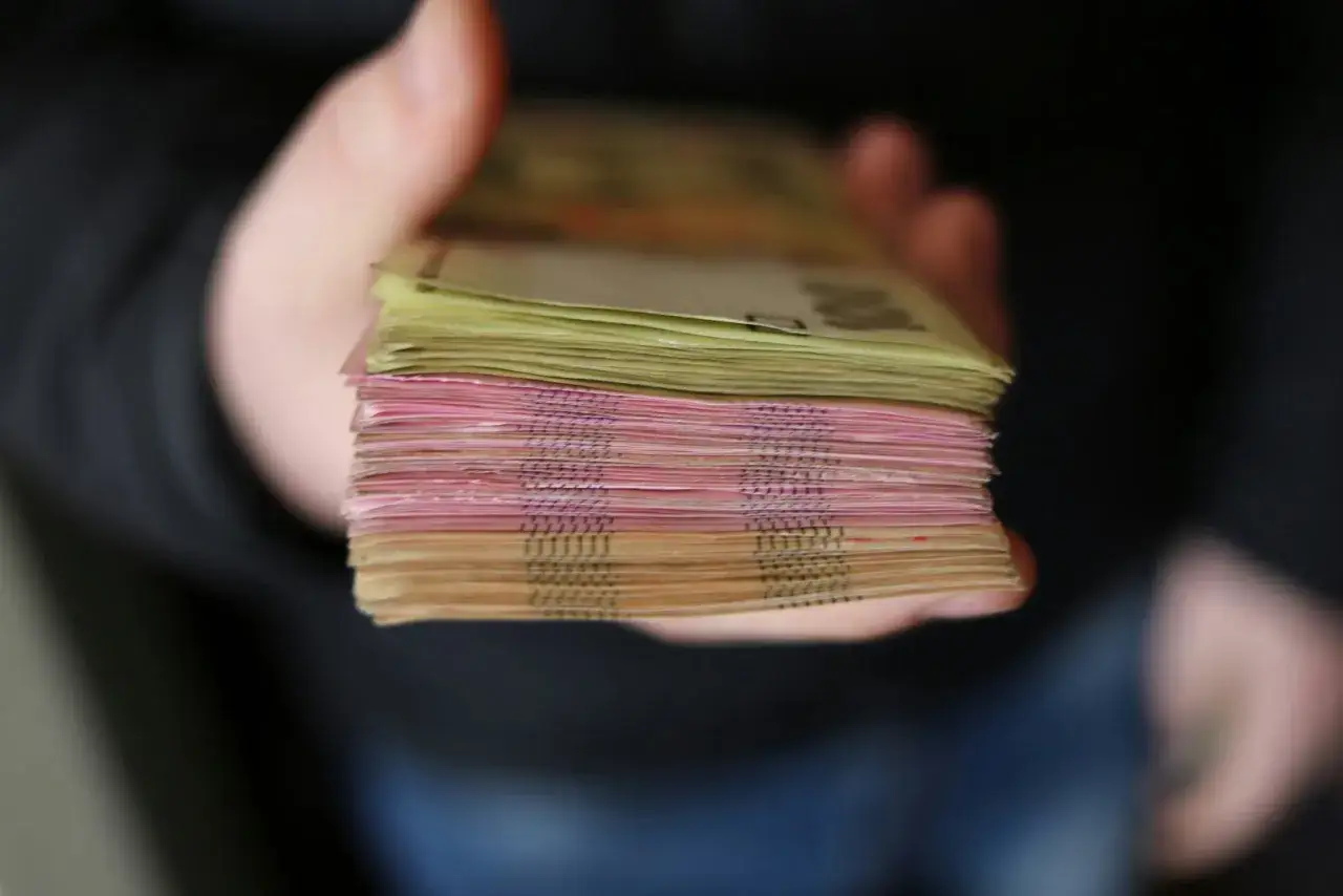 Gruba paczka banknotów, różowych i żółtych, trzymana w dłoni. To pewne zabezpieczenie finansowe.