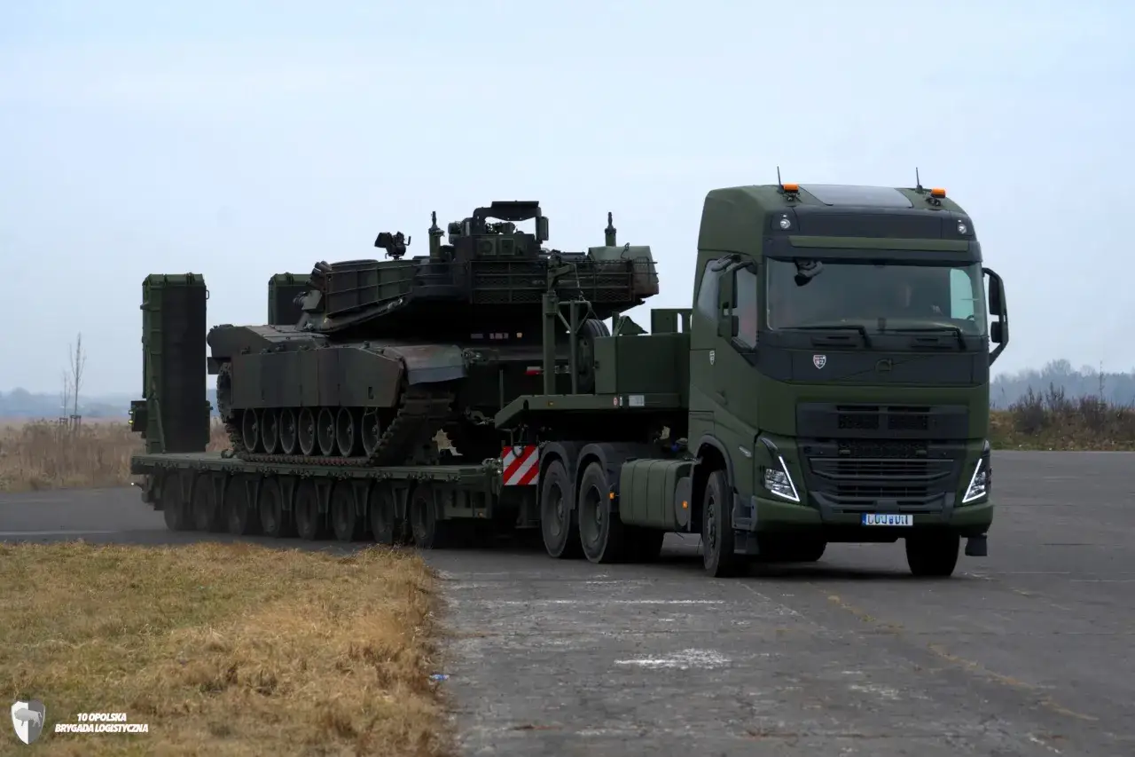Ciężarówka Volvo FH16 w wojskowym kamuflażu transportuje czołg na lawecie.