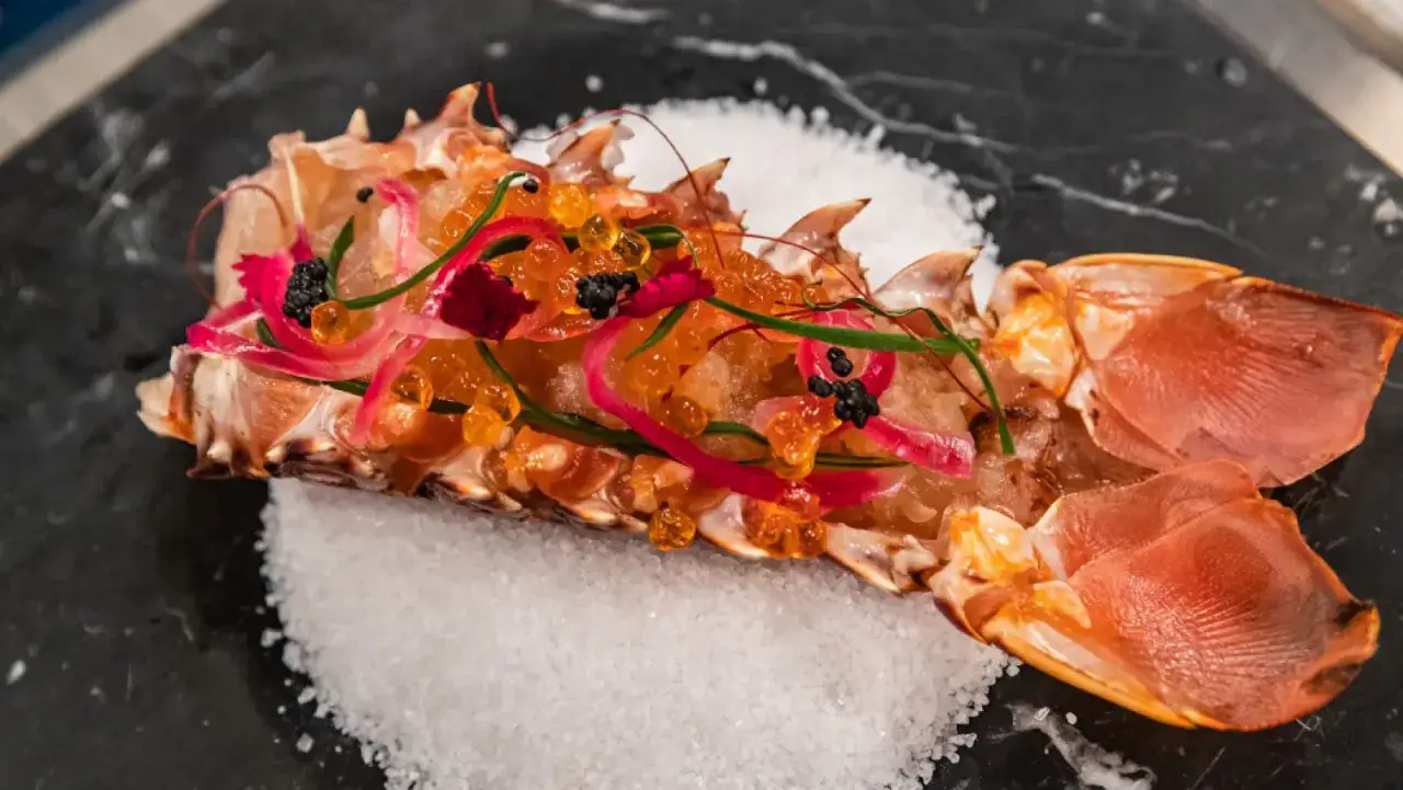 Delicioso langosta marisco servido sobre sal gruesa, adornado con huevas naranjas, cebolla morada y caviar negro.