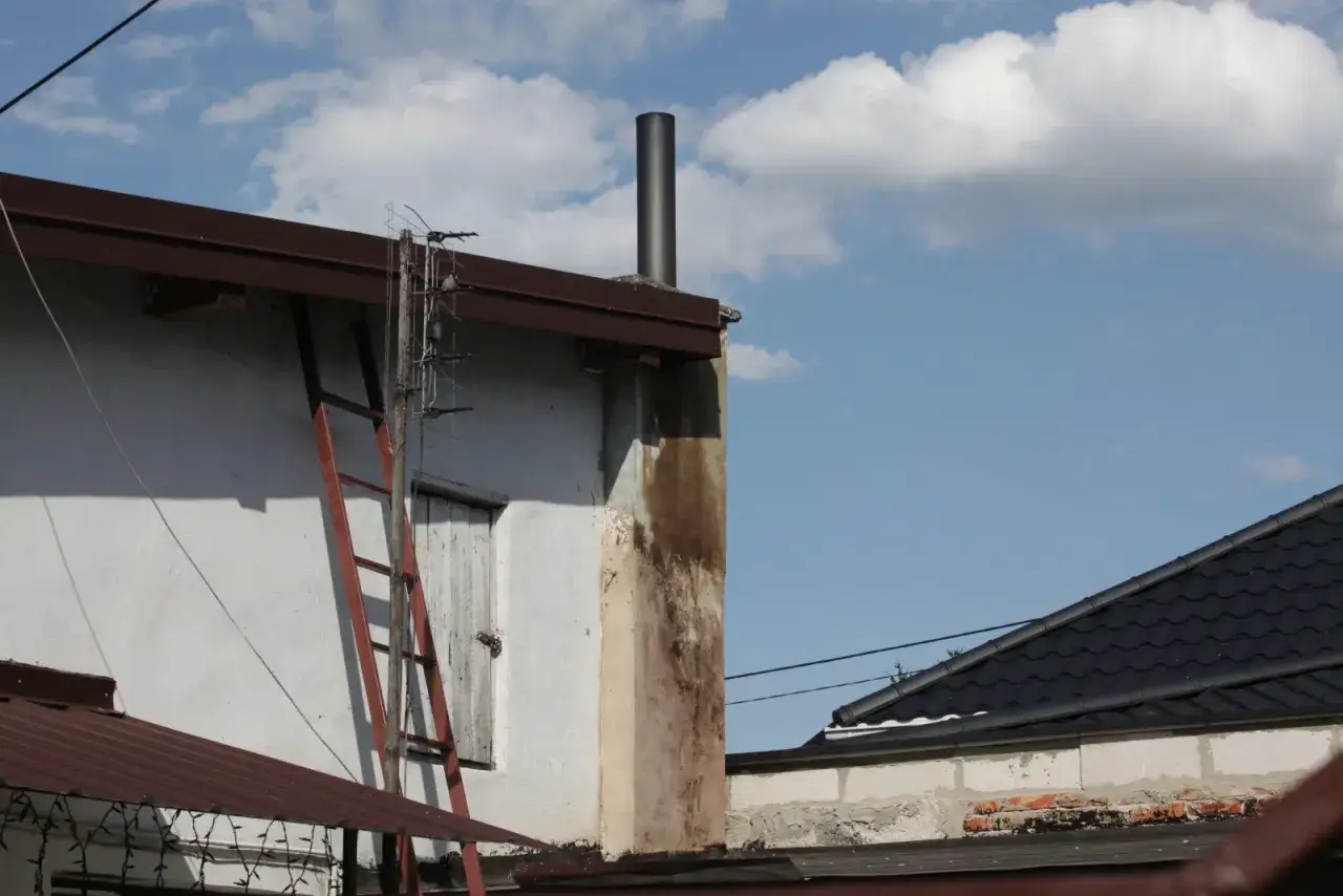 Nowy, czarny komin zewnętrzny do pieca na pellet wystaje ponad dach. Obok drabina i stara antena.