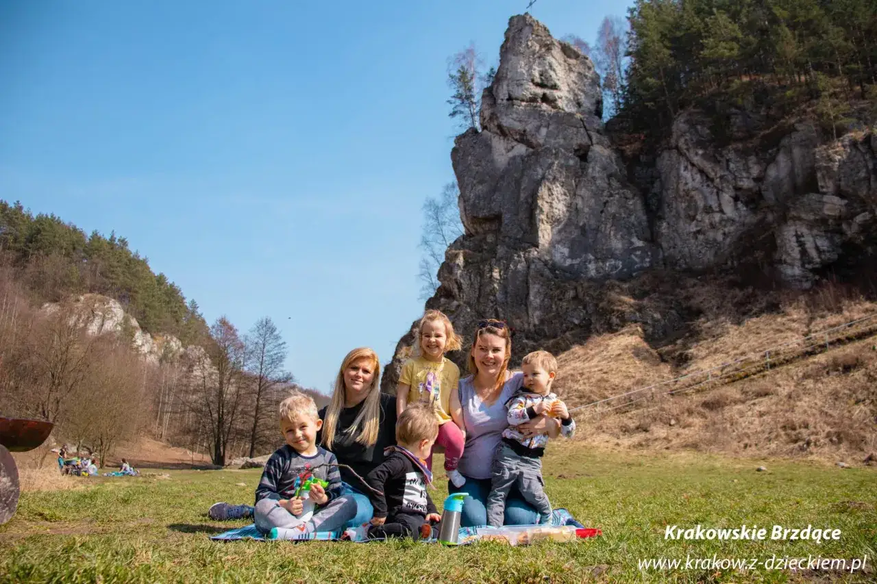 Rodzina na pikniku w Dolinie Kobylańskiej. Dzieci i dwie kobiety siedzą na kocu przed skalistym zboczem.