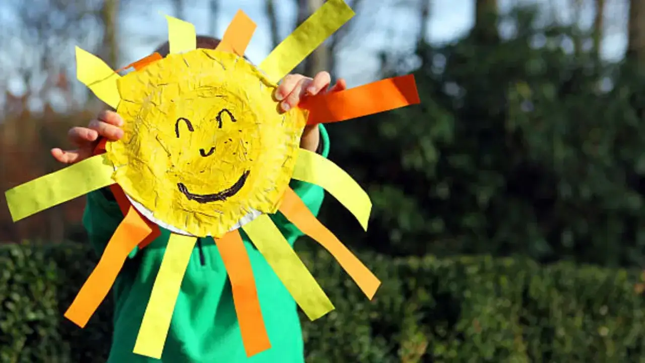 Un ni&ntilde;o sonriente sostiene un sol de papel, una de las muchas actividades infantiles de verano.
