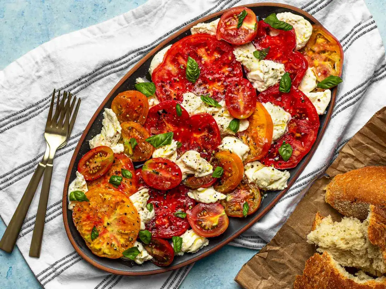 En vacker caprese sallad med skivade tomater i olika färger, färsk mozzarella och basilika. Serveras på ett fat med bröd.