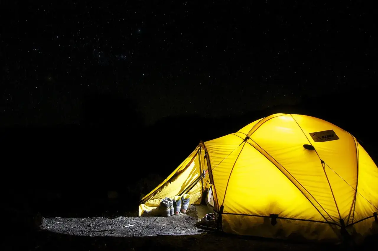 Ein leuchtend gelbes Zelt f&uuml;r **wild camping** unter einem sternenklaren Nachthimmel. Wanderschuhe stehen bereit.