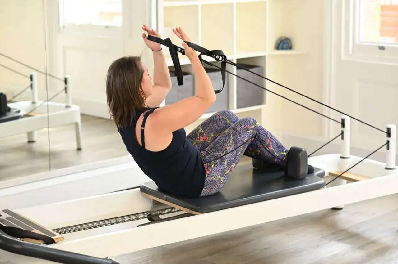 Kobieta ćwiczy na reformerze pilates. Czy pilates odchudza? Tak, regularne ćwiczenia wzmacniają ciało i mogą pomóc w redukcji wagi.