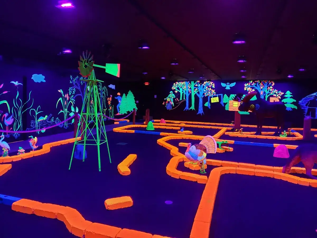 Ein leuchtendes indoor schwarzlicht minigolf Abenteuer mit bunten Hindernissen, einer Windm&uuml;hle und Tierfiguren.
