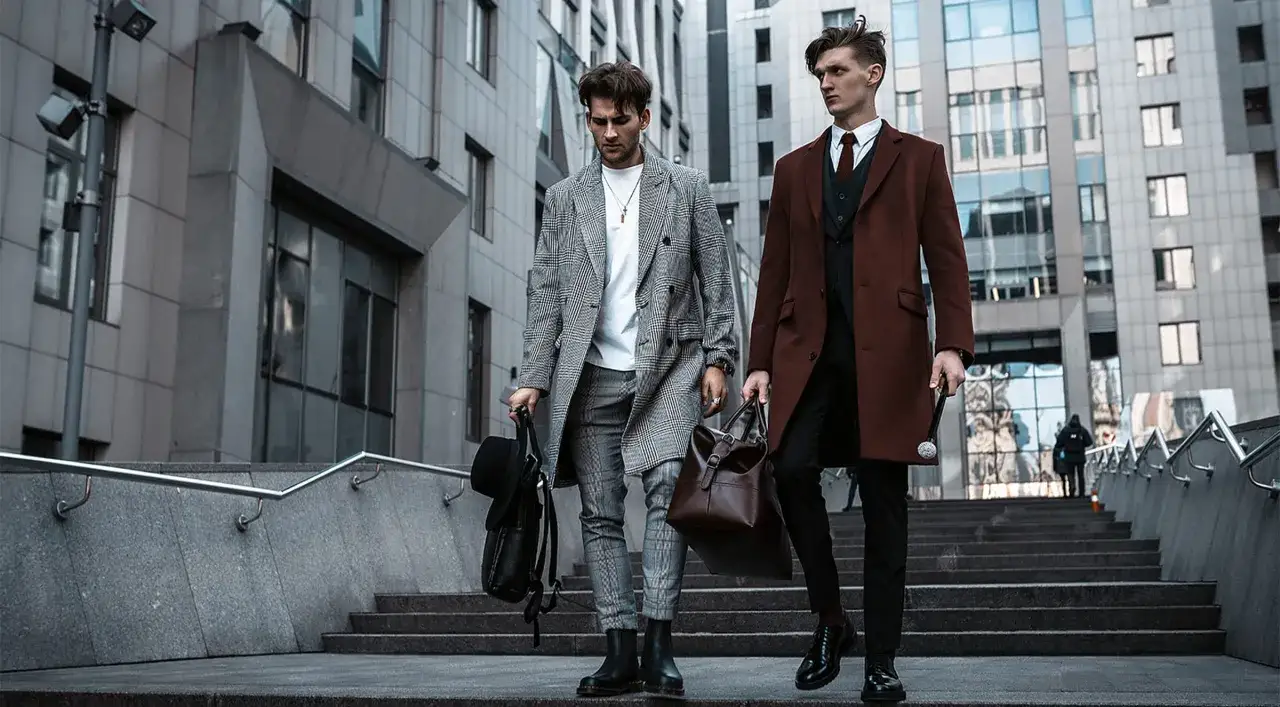 Zwei Männer in **smart business attire** gehen eine Treppe hinauf. Einer trägt einen karierten Mantel, der andere einen braunen Mantel.