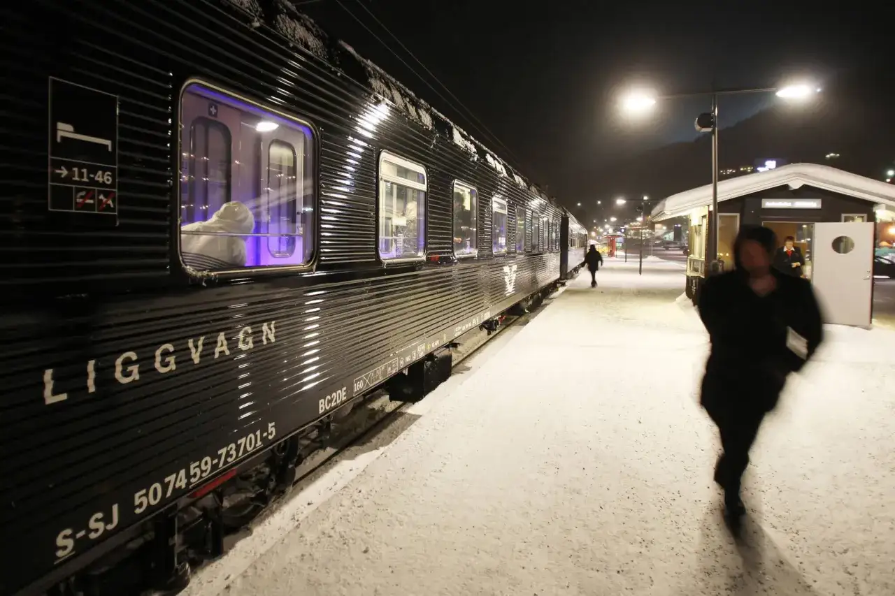 Ett m&ouml;rkt liggvagnst&aring;g st&aring;r p&aring; en sn&ouml;t&auml;ckt station. Kanske &auml;r det p&aring; v&auml;g mot Berlin fr&aring;n Stockholm.