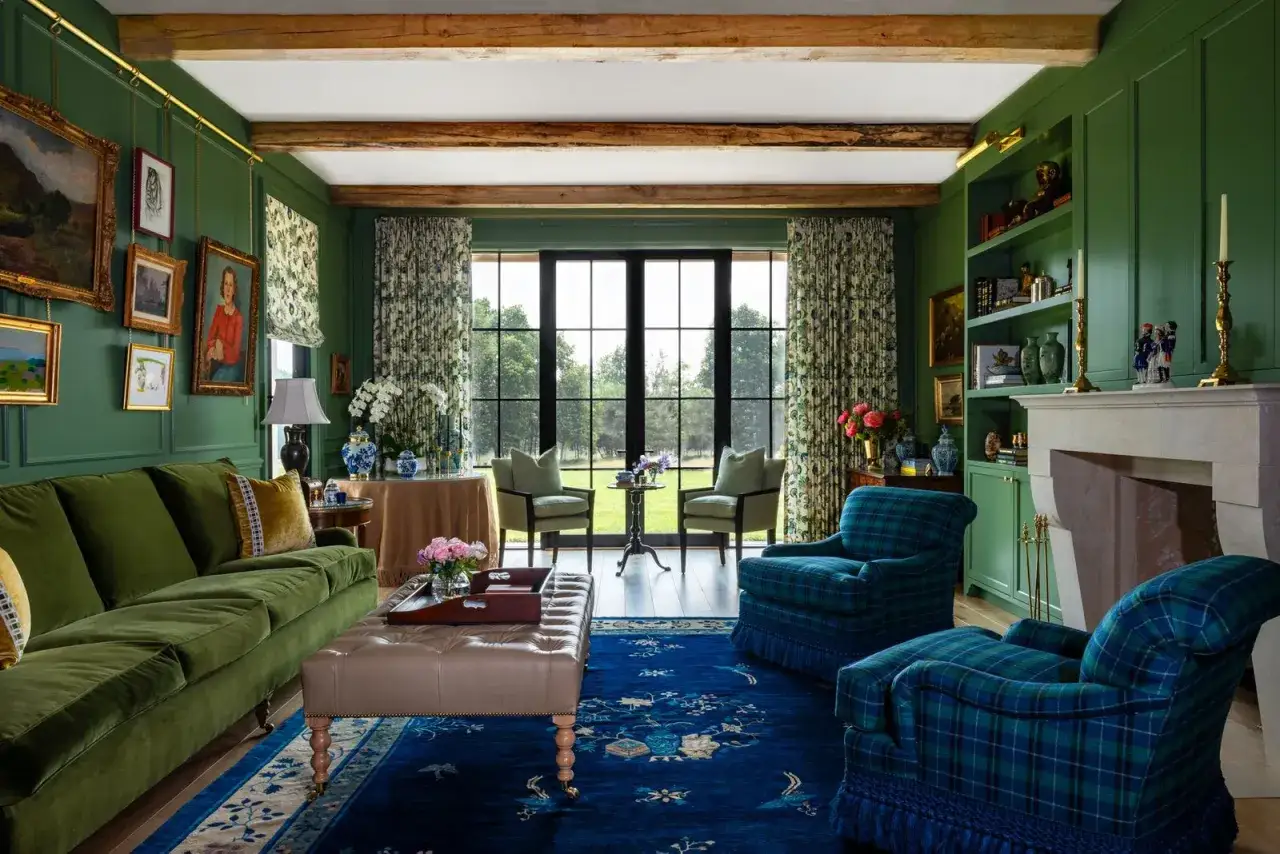 A luxurious living room with millenial green walls, a plush green sofa, tartan armchairs, and a large window overlooking a garden.