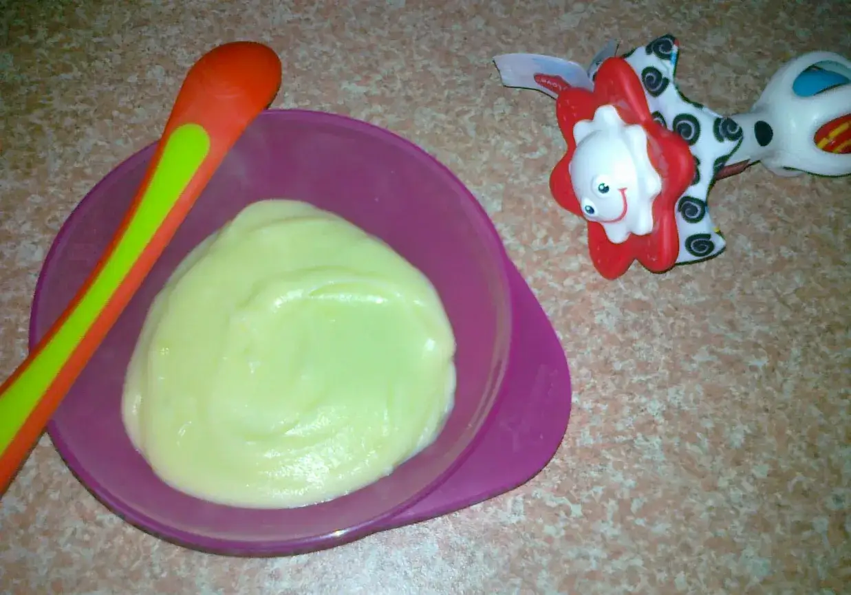 Jak przygotować ziemniaka dla niemowlaka? Miseczka z puree ziemniaczanym, pomarańczowo-zielona łyżeczka i zabawka dla dziecka.
