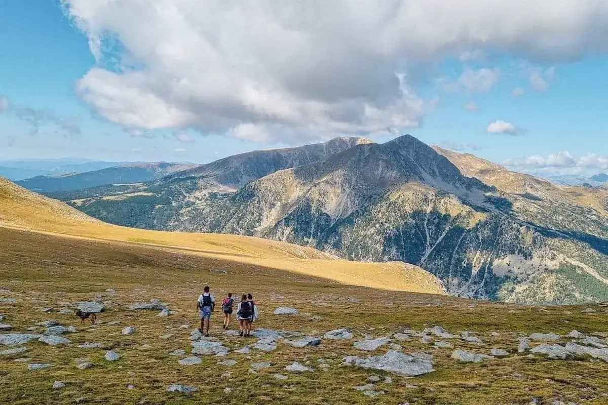 Hikers with backpacks explore a vast, rocky landscape with a dog, enjoying the stunning mountain views of hiking the Pyrenees, Spain.