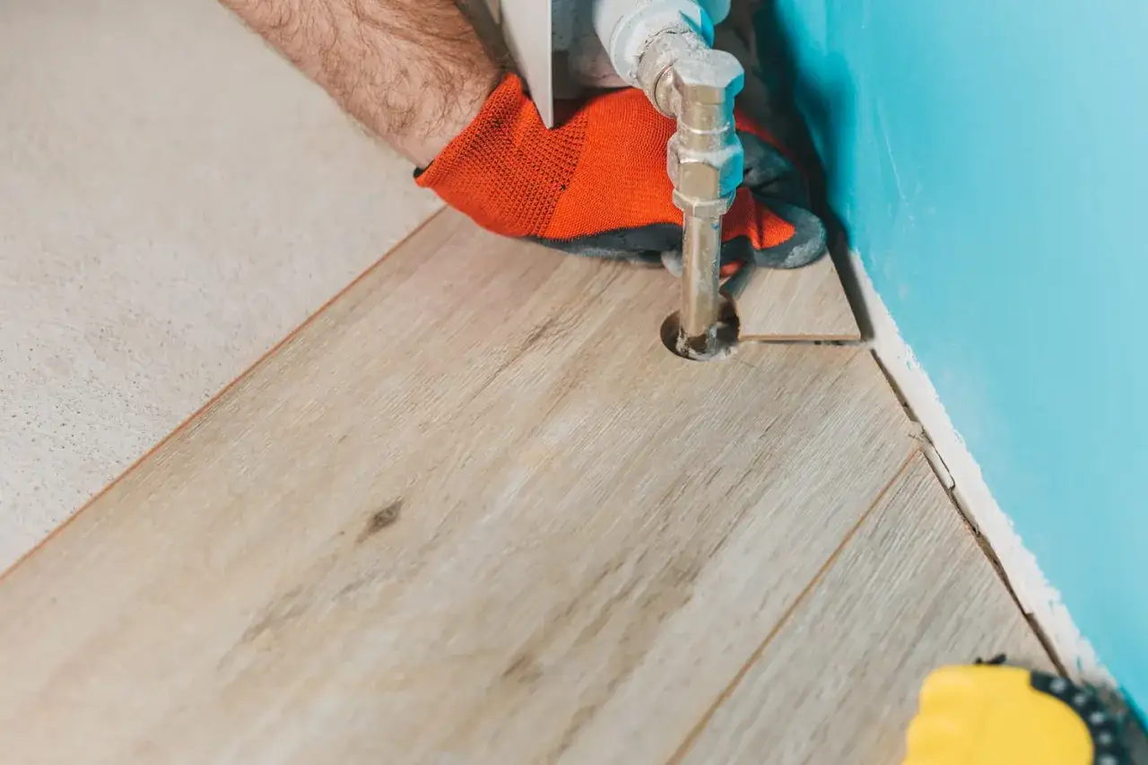 Main tenant effectuant une d&eacute;coupe parquet autour d'un tuyau de chauffage.