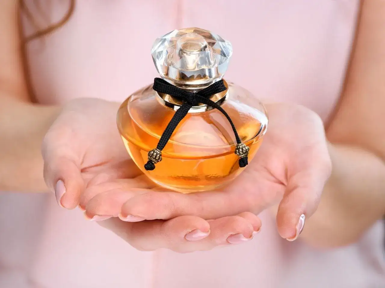 Eleganckie perfumy lat 90 damskie w szklanej buteleczce z czarną wstążką, trzymane w dłoniach.
