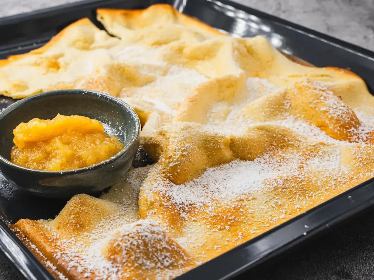 Omas Pfannkuchen-Rezept: Ein goldbrauner, luftiger Pfannkuchen mit Puderzucker bestäubt, serviert mit Apfelmus.