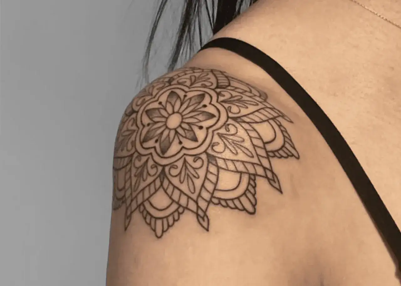 Delikatny, czarny **mandala tatuaż** zdobi ramię kobiety, tworząc subtelny wz&oacute;r.