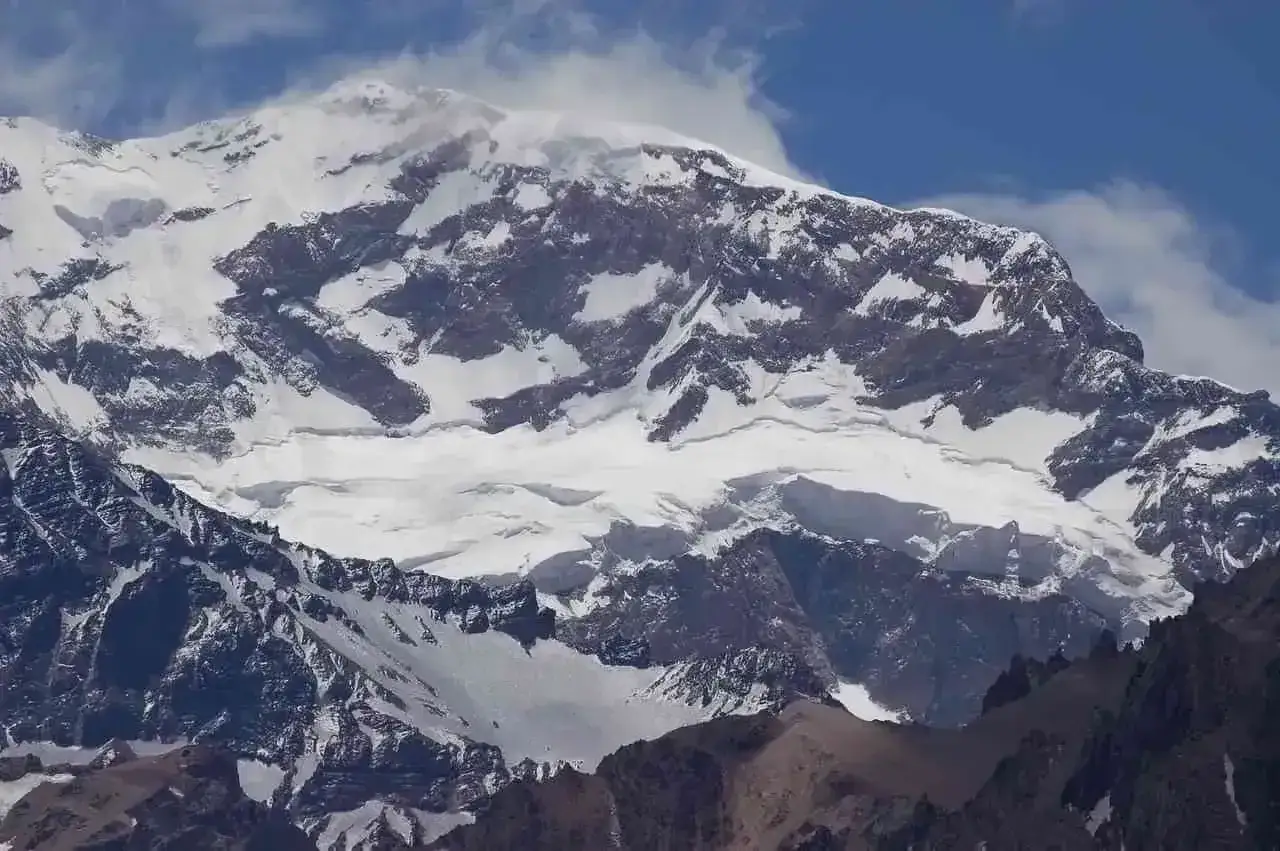 Majestatyczne góry z Aconcagua, pokryte śniegiem i lodem, wznoszą się ku błękitnemu niebu z kłębiącymi się chmurami.