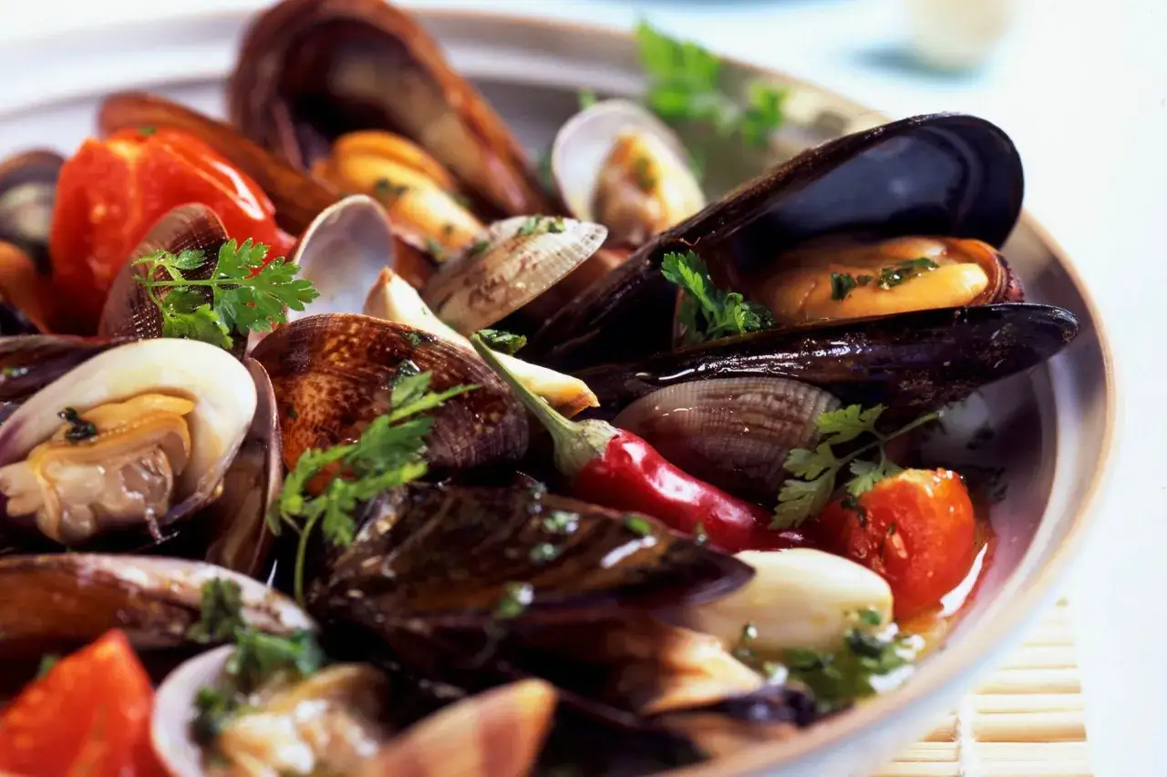 Un invitante sugo cozze e vongole, con pomodorini, peperoncino e prezzemolo fresco, pronto per essere gustato.