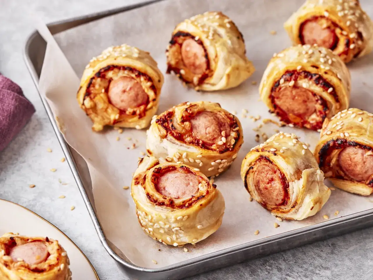 Leckere bratwurst im schlafrock, goldbraun gebacken und mit Sesam bestreut, liegen auf einem Backblech.