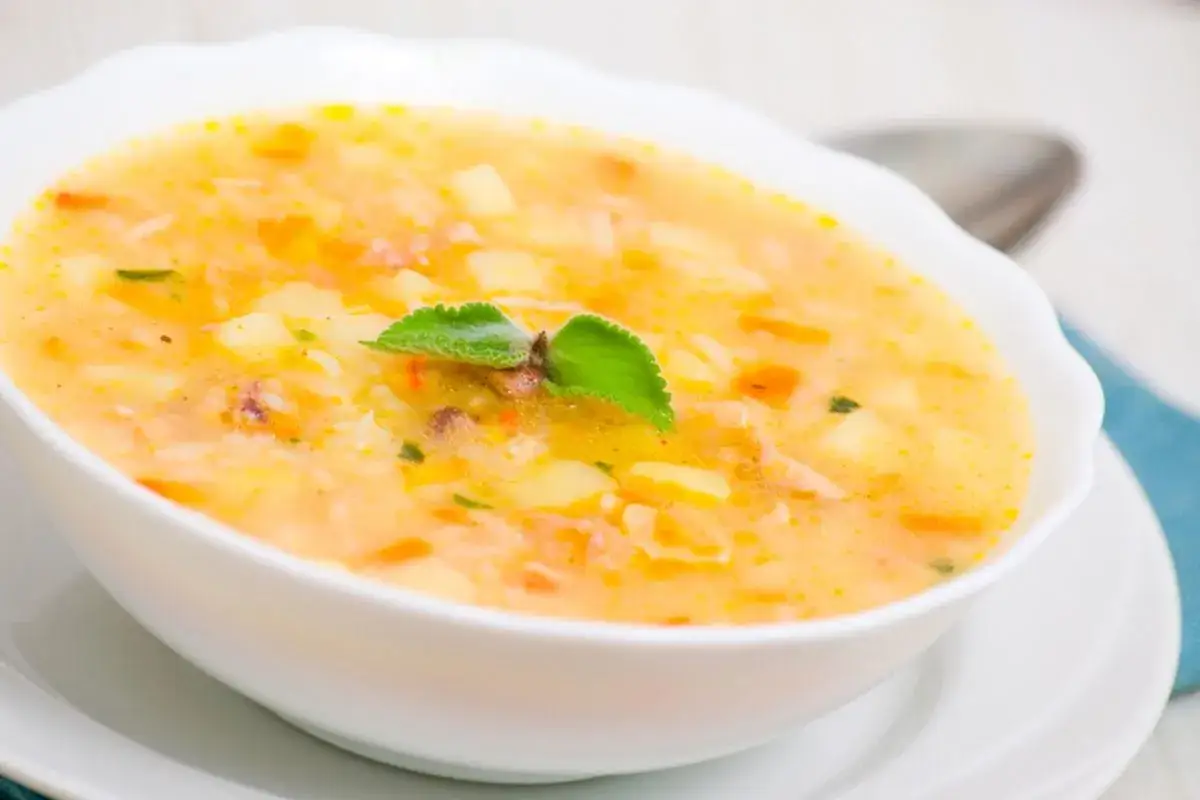 Una ciotola di zuppa cremosa con pezzi di riso e patate, guarnita con una foglia verde.