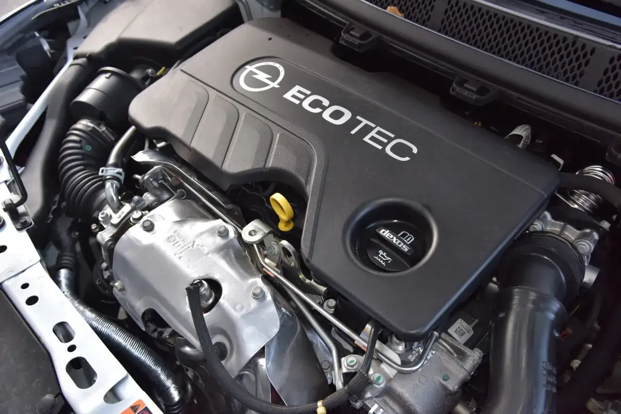 Silnik Ecotec w Oplu Astra K 1.6 CDTI. Widoczny czarny plastik z logo Opla i napisem Ecotec, żółta miarka oleju i czarny korek z napisem Dexos.