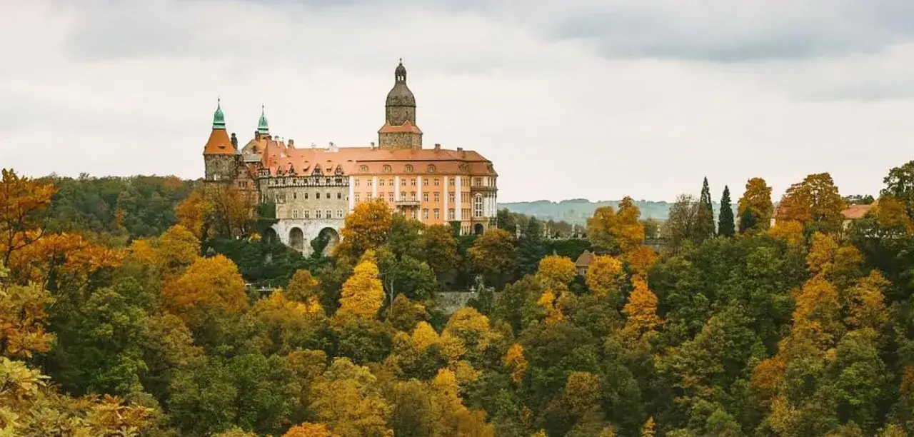 Schloss F&uuml;rstenstein in Niederschlesien, umgeben von herbstlich gef&auml;rbten B&auml;umen.