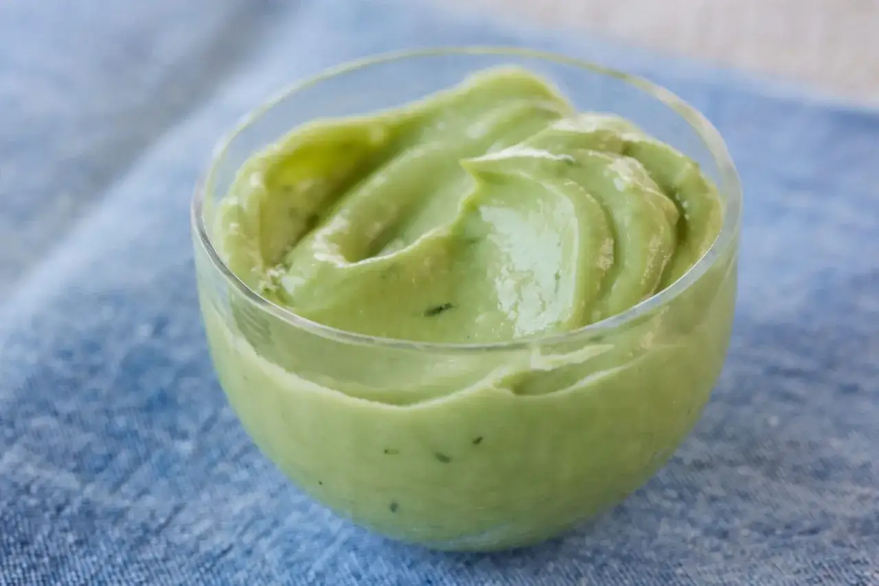 Una cremosa maionese di avocado, servita in una coppetta di vetro su un tovagliolo blu.