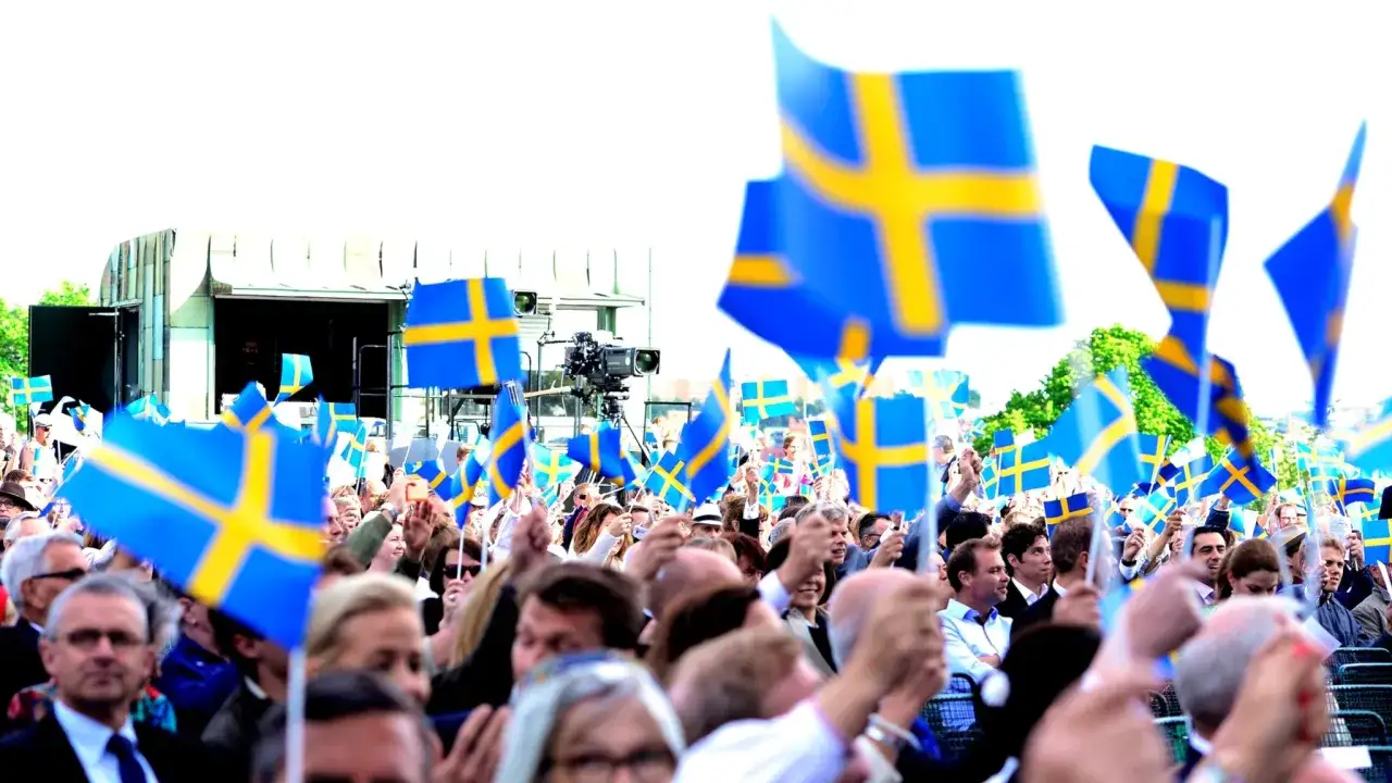 Stor folkmassa viftar med svenska flaggor. Vad heter svenska flaggan? Den heter Sveriges flagga.