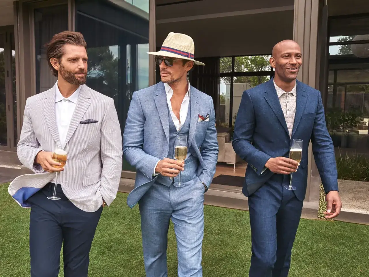 Three stylish men in suits holding champagne glasses. This image asks: do you have to wear a suit to a wedding?