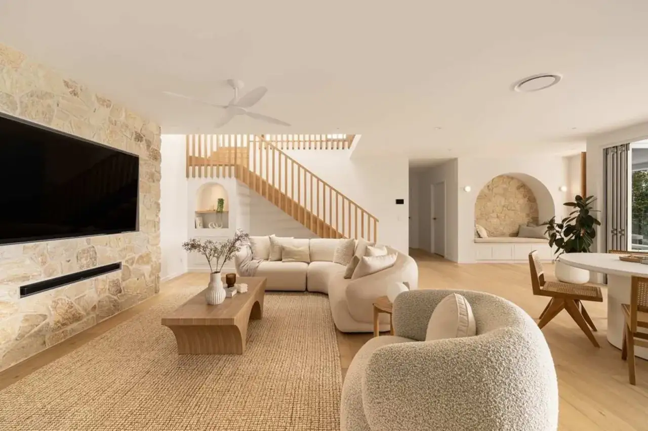 Moderne Wohnlandschaft mit einem geschwungenen Sofa als Raumteiler. Ideen für ein gemütliches Wohnzimmer mit Steinwand und Holztreppe.