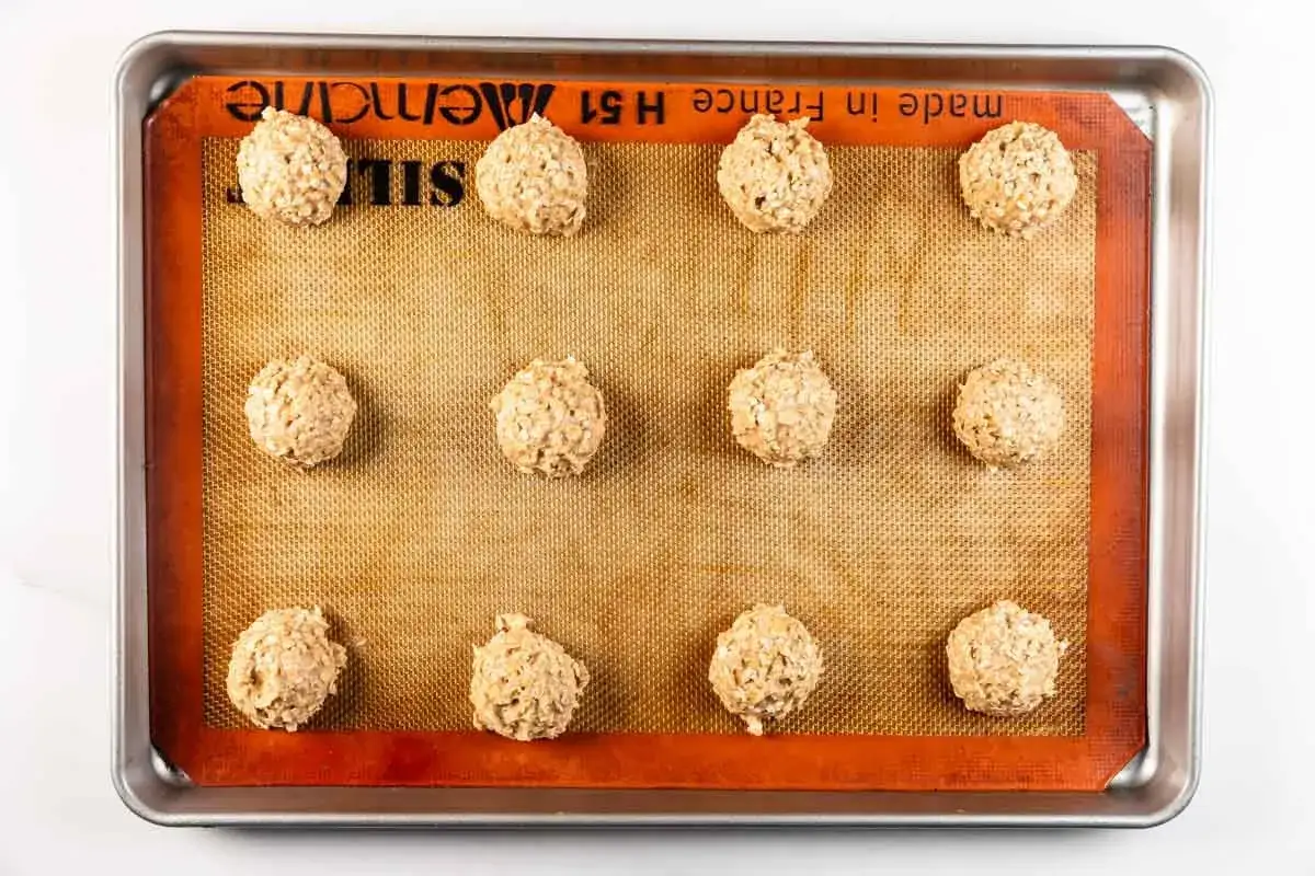 Zw&ouml;lf rohe bananen haferflocken kekse liegen auf einem Backblech mit Silikonmatte bereit zum Backen.