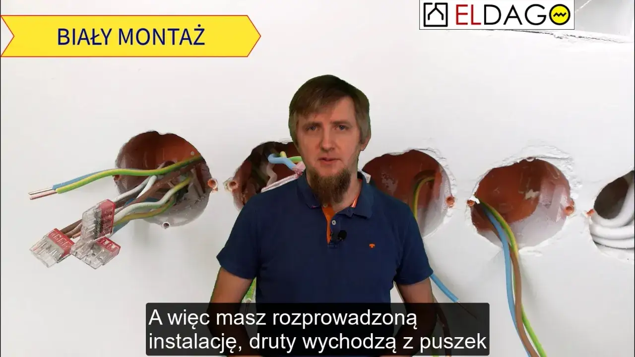 Elektryk pokazuje instalację elektryczną w ścianie. Dowiedz się, ile kosztuje biały montaż elektryczny i jak wygląda rozprowadzanie przewodów.
