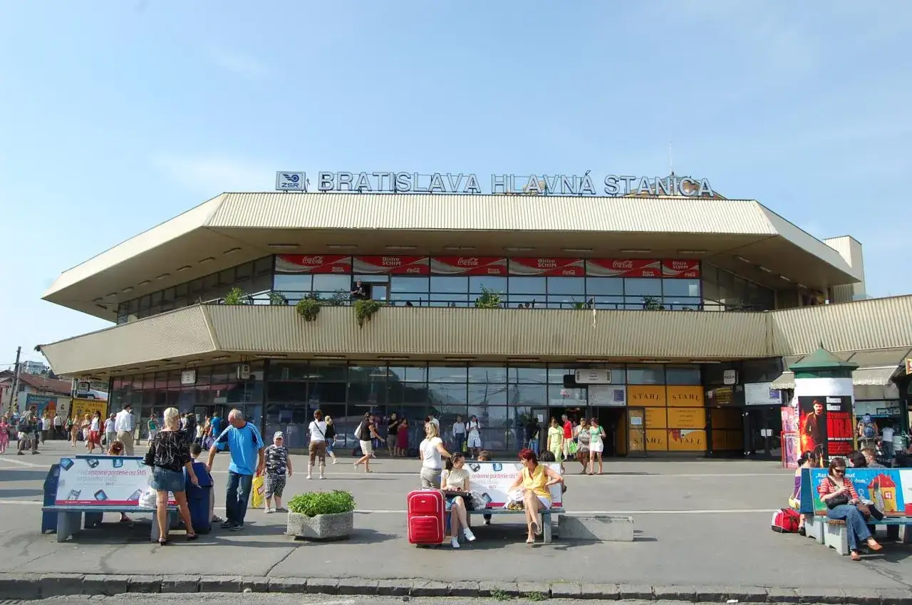 Menschen warten vor dem Bratislava Hlavná Stanica, dem Hauptbahnhof von Bratislava, unter einem blauen Himmel.
