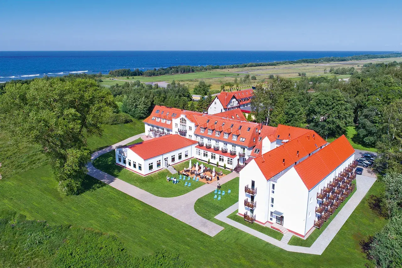 Hotel Mona Lisa Kołobrzeg z widokiem na morze. Białe budynki z czerwonymi dachami, otoczone zielenią.
