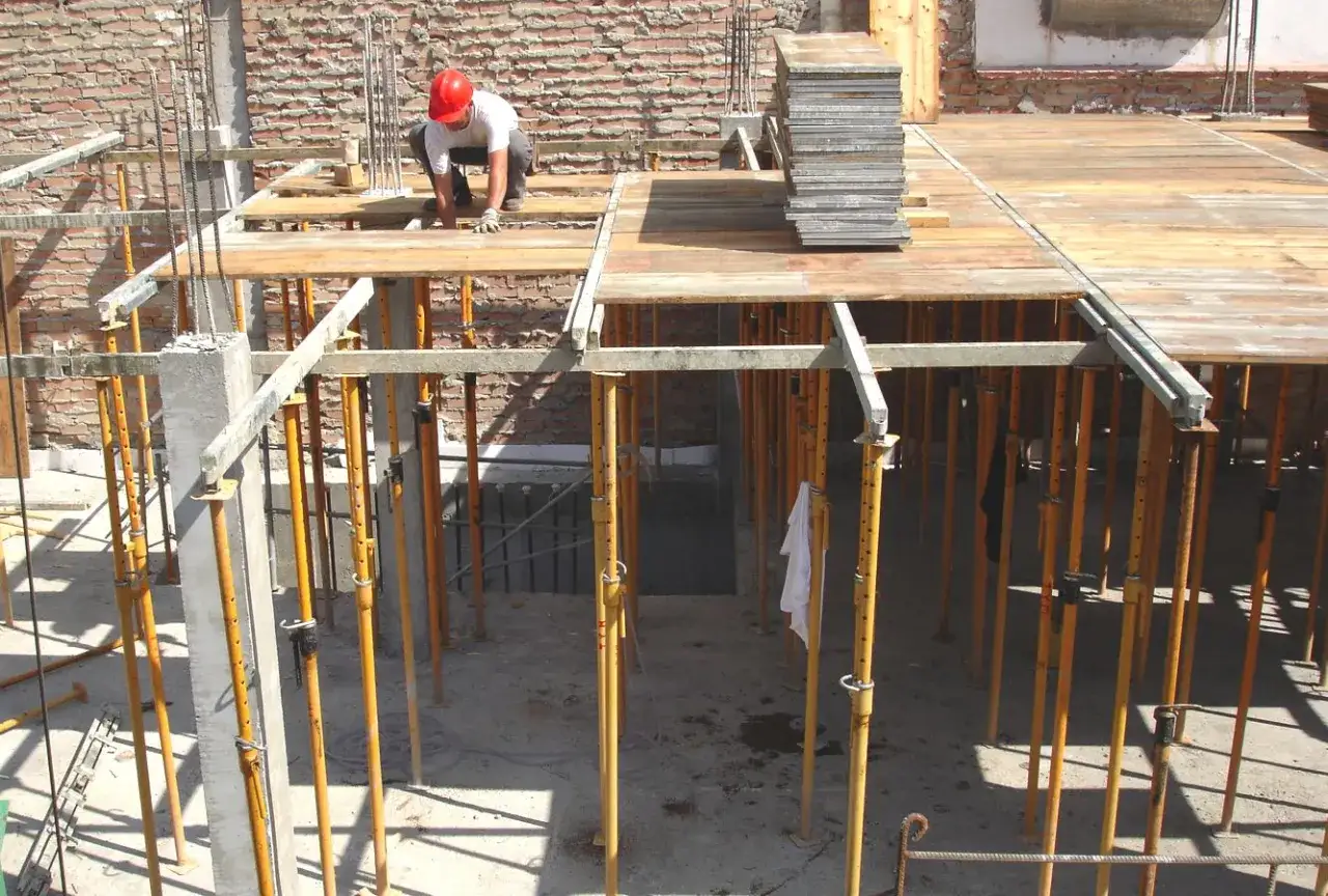 Obrero trabajando en una obra, instalando la cimbra de madera y soportes met&aacute;licos para una losa.