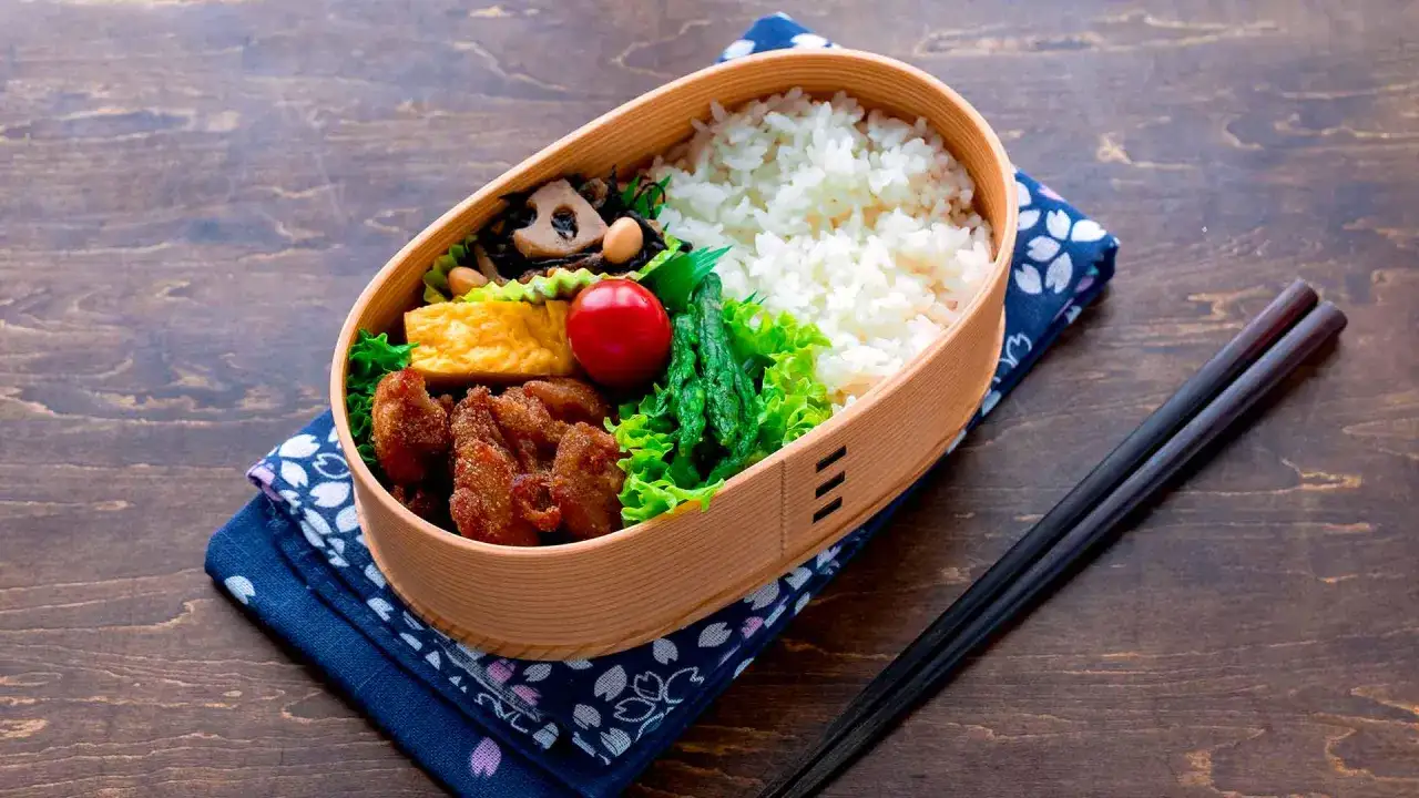 A delicious rice bento box filled with fried chicken, tamagoyaki, vegetables, and rice, ready for a satisfying meal.
