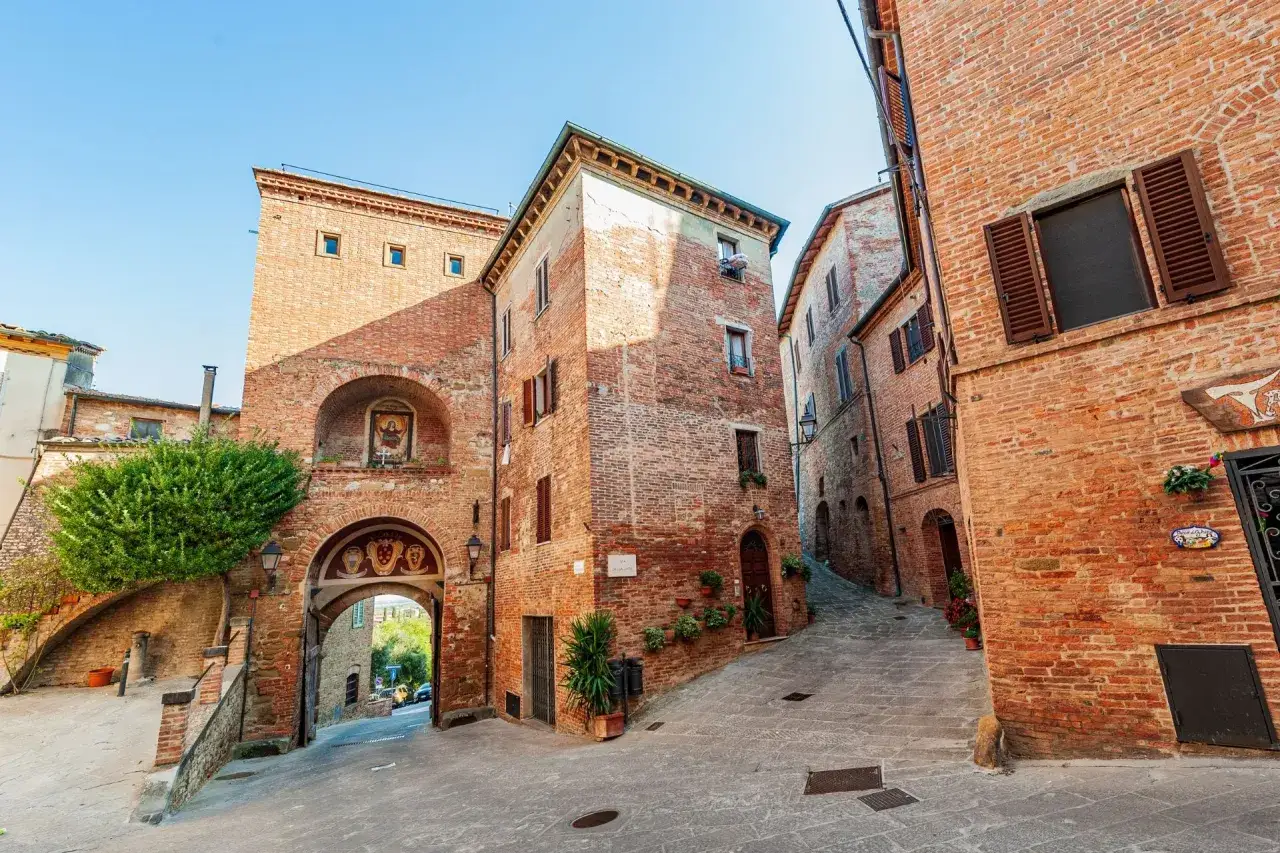 Un vicolo acciottolato a Torrita di Siena, con edifici in mattoni rossi e un arco medievale.