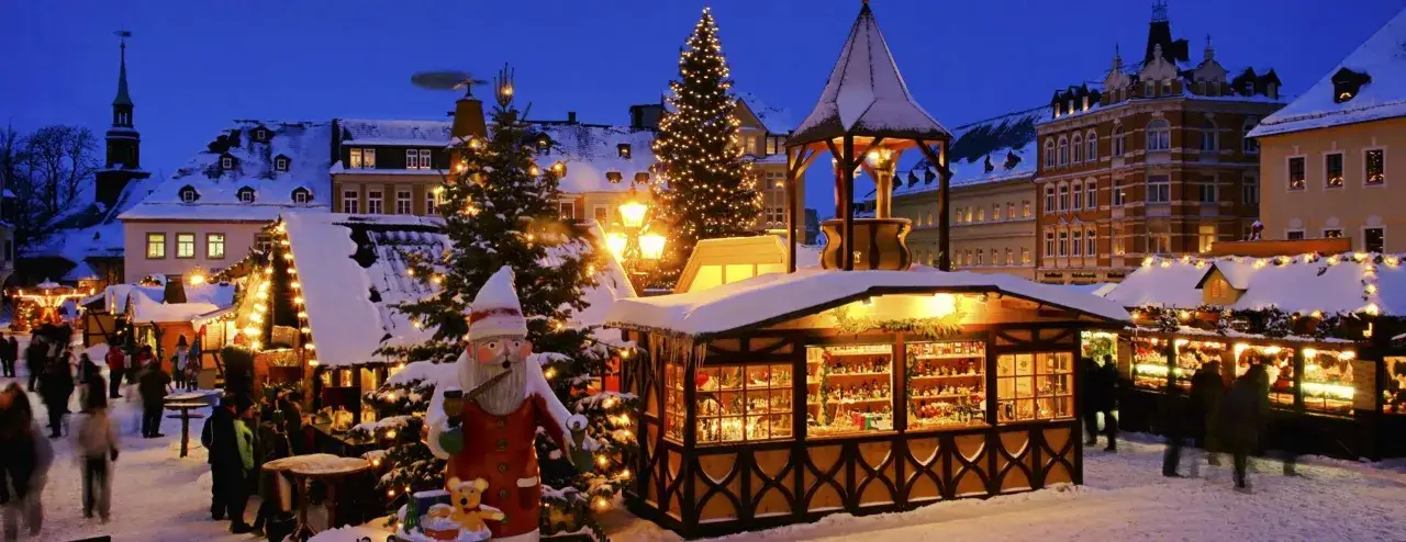 Ein verschneiter Weihnachtsmarkt im Dezember mit beleuchteten Tannenbäumen, Buden und einer großen Weihnachtsmannfigur. Perfekt für einen winterlichen Urlaub.