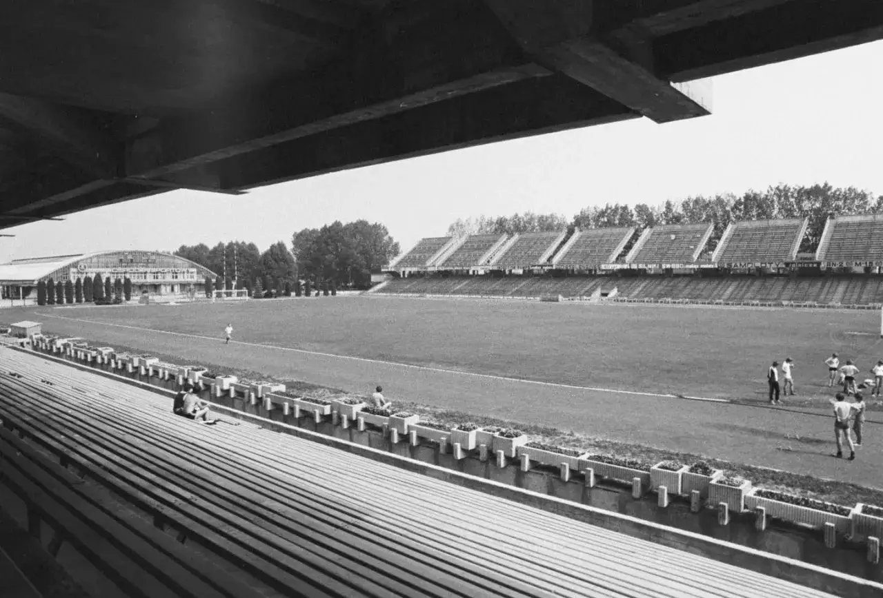 Widok na stary stadion Stali Mielec z trybun. Na boisku widać kilku piłkarzy, a w tle budynek klubowy i drzewa.
