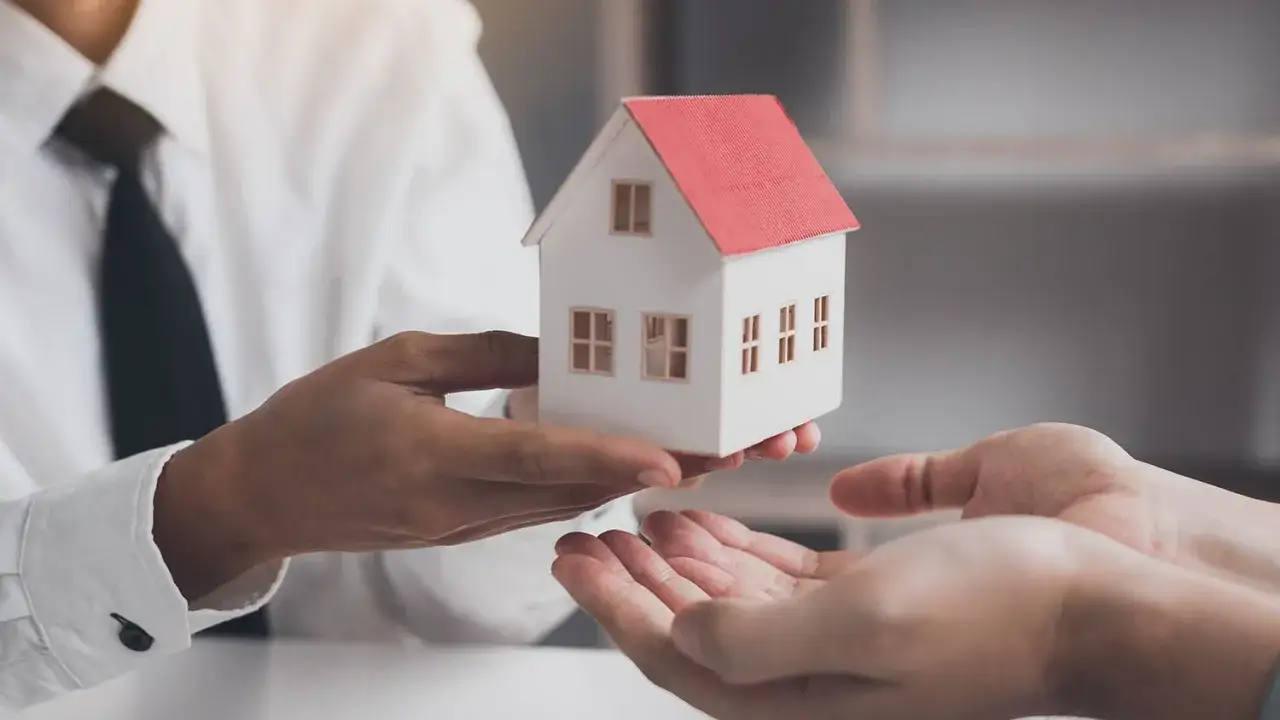 Man entrega una maqueta de casa, simbolizando que es obligatorio tener seguro de hogar para proteger tu inversión.