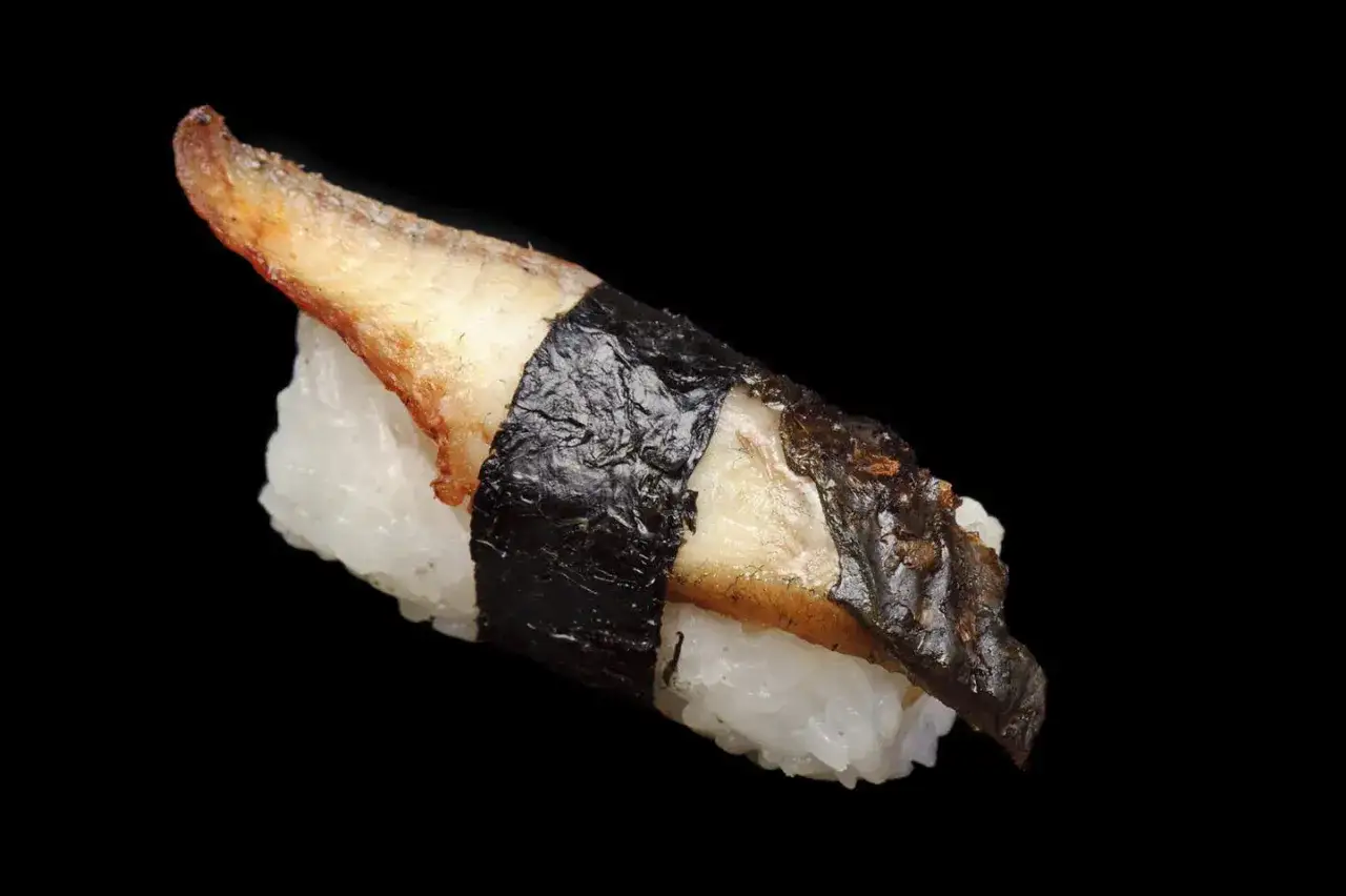Nigiri z pieczonym węgorzem do sushi, owinięte nori, na czarnym tle.