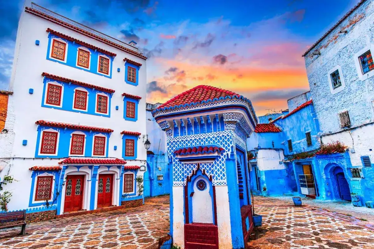 Callejuela de la marruecos ciudad azul, con casas blancas y azules, tejados rojos y un cielo anaranjado al atardecer.