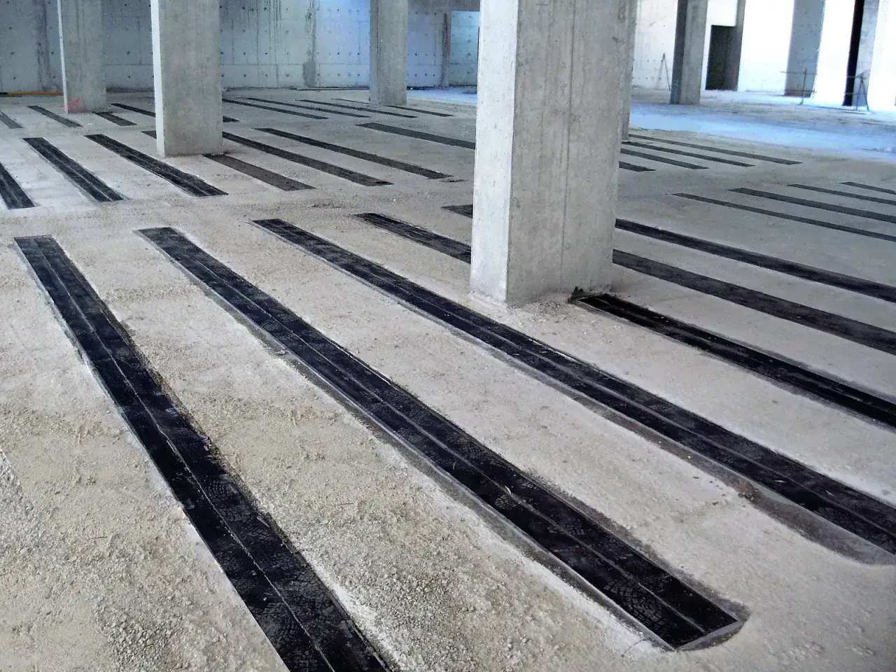 Suelo de hormig&oacute;n con tiras negras incrustadas, parte de un proyecto de refuerzo estructural.