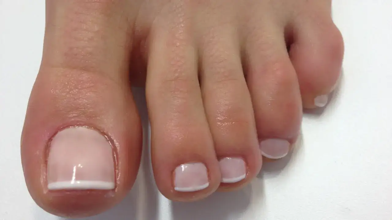 Zadbany pedicure french na stopach, z delikatnym różowym lakierem i białymi końcówkami.