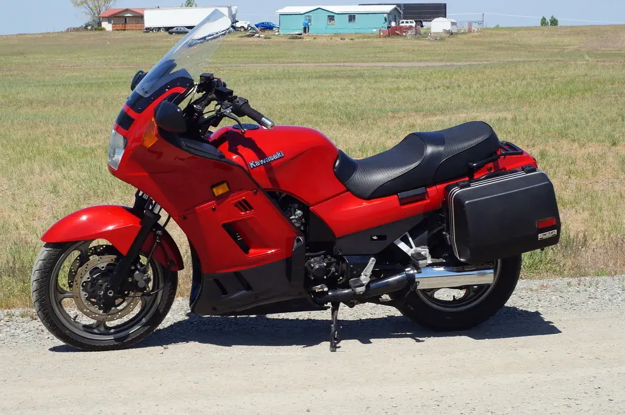 Czerwony Kawasaki GTR 1000 z czarnymi kuframi, gotowy na długie trasy pośród pól.