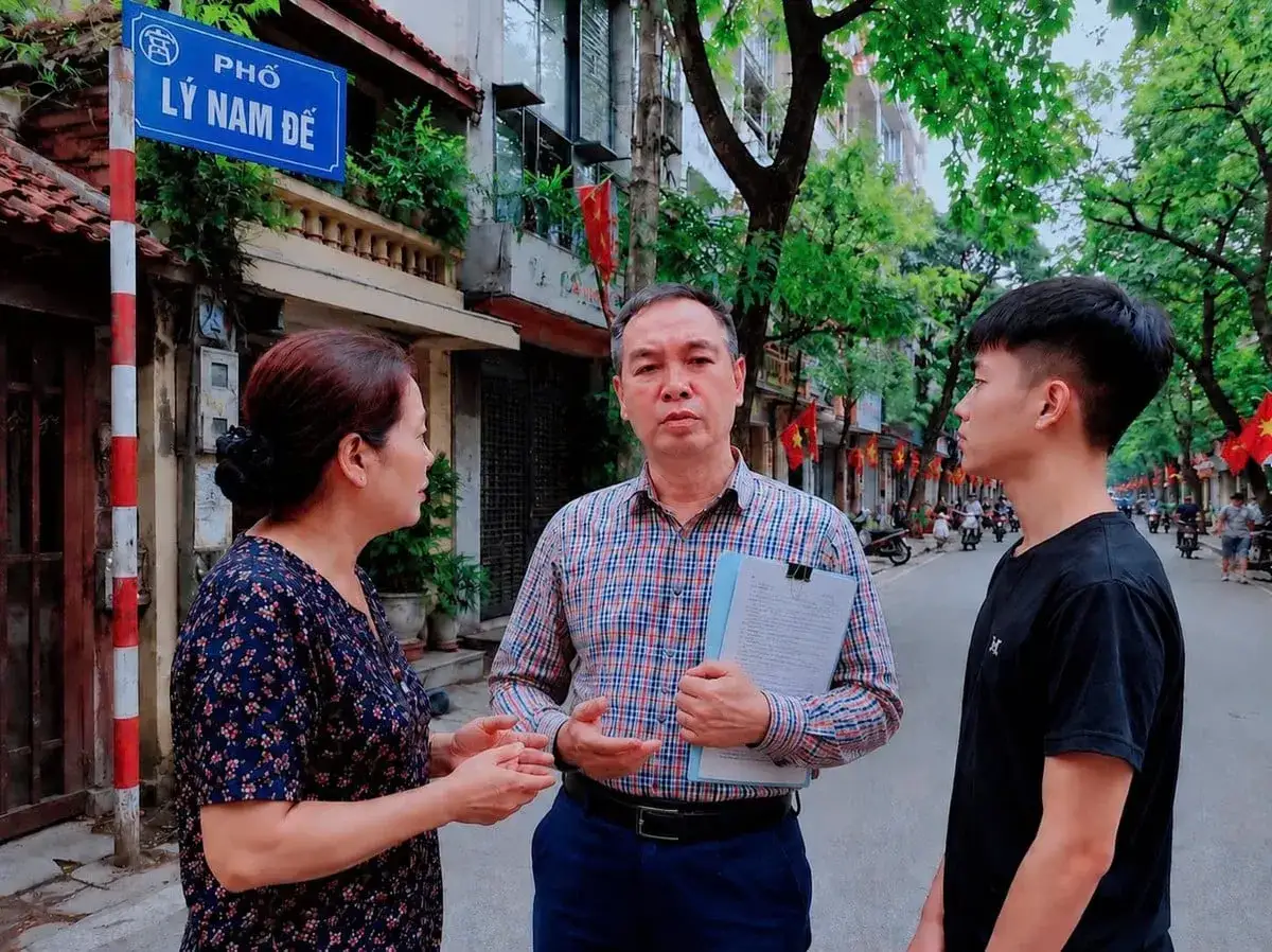 Na ulicy L&yacute; Nam Đế w Hanoi, tr&oacute;jka os&oacute;b rozmawia. Mężczyzna trzyma dokumenty, a obok niego stoi młody chłopak. To pokazuje, jakie są wietnamki - dumne i zaangażowane.