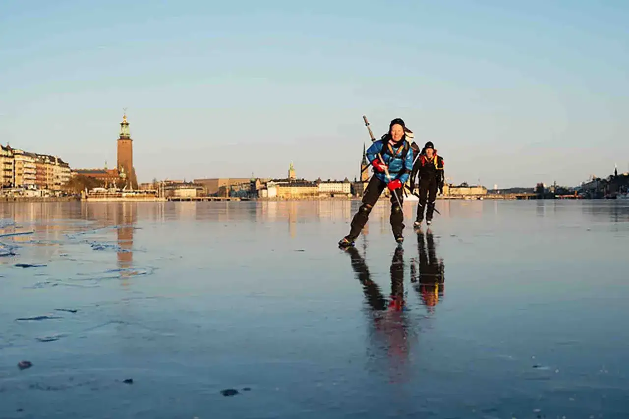 Två personer skridskor på isen med Stockholms stadshus i bakgrunden. En fantastisk upplevelse i Sverige.