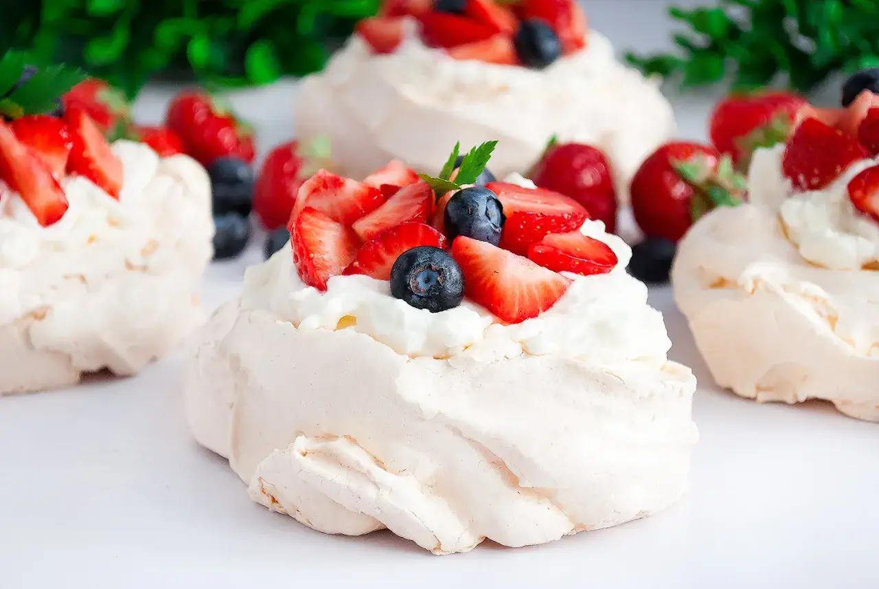 Mini bezy pavlova z bitą śmietaną, truskawkami i borówkami. Pyszny deser na letnie popołudnie.
