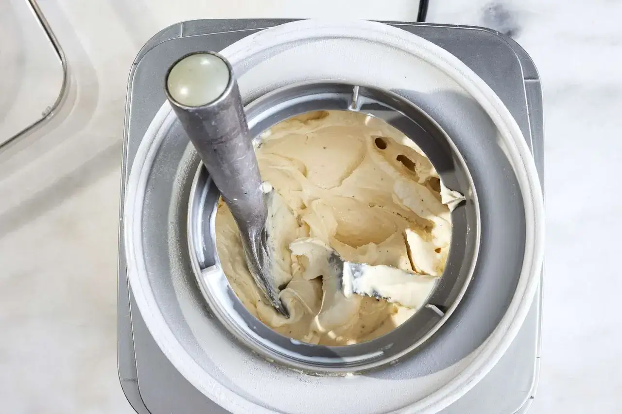 Cremiges Vanilleeis wird in einer Eismaschine zubereitet. Der Rührarm verteilt die Masse.
